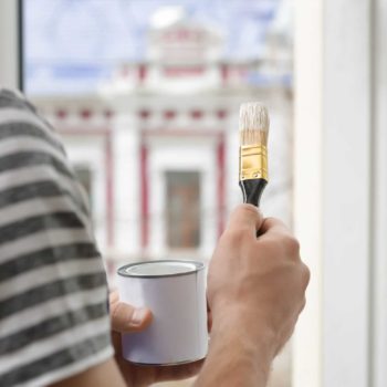man painting window frames with a brush