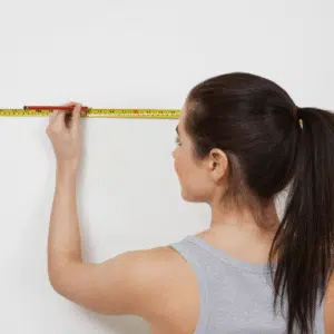 Lady measuring a wall and marking it with a pencil.
