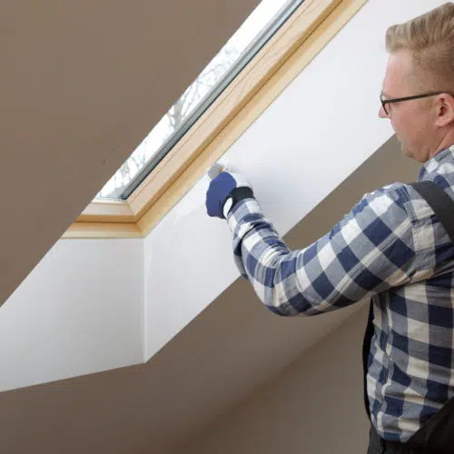 Decorator cutting in with a paint brush around a window frame