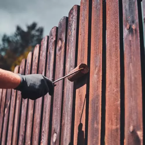 person painting a fence on a cloudy day